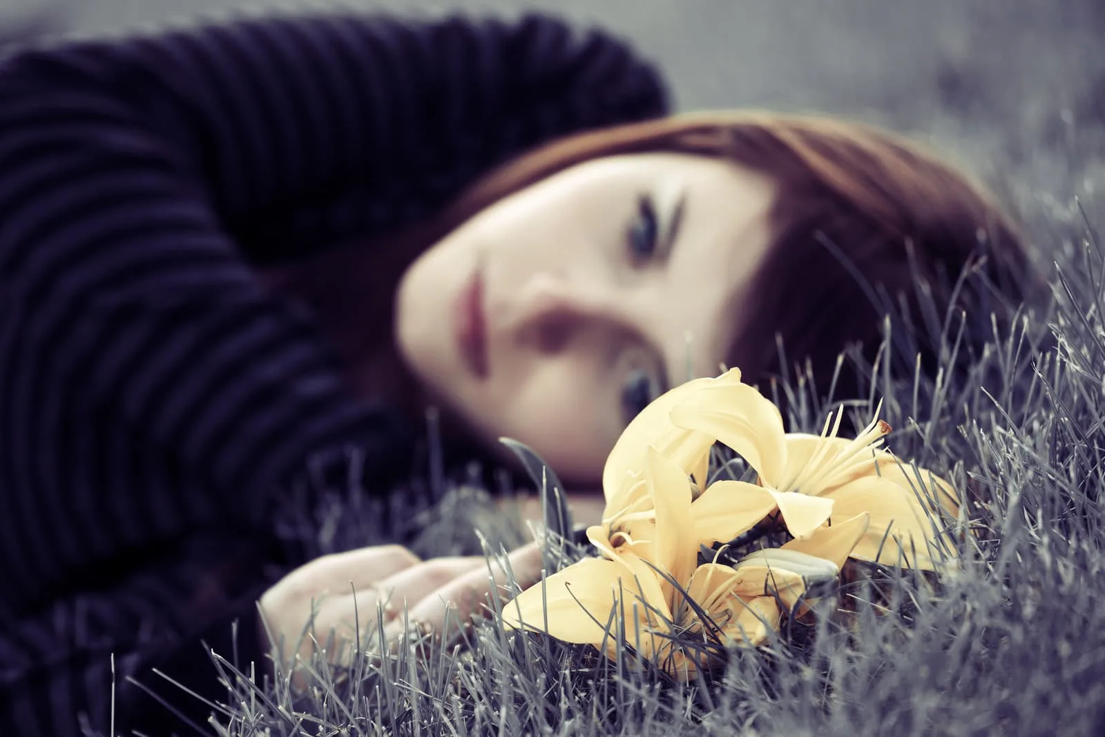 a sad girl lying in the grass with a yellow flower in her hand