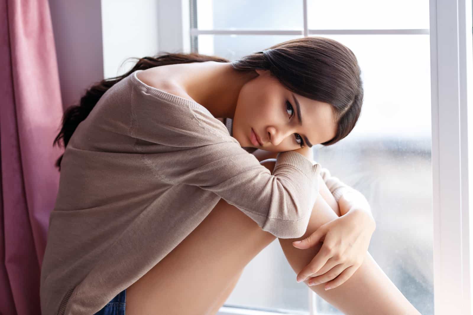 una mujer triste está sentada junto a la ventana