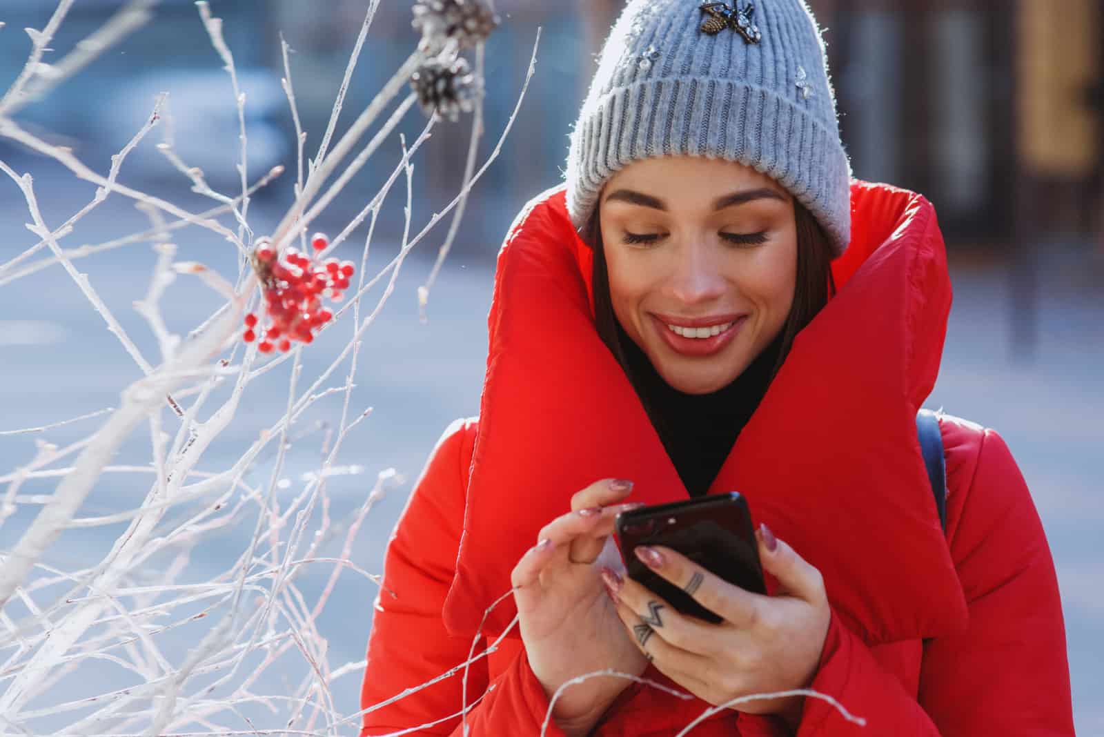 uma morena sorridente com um casaco de peles vermelho utiliza um smartphone