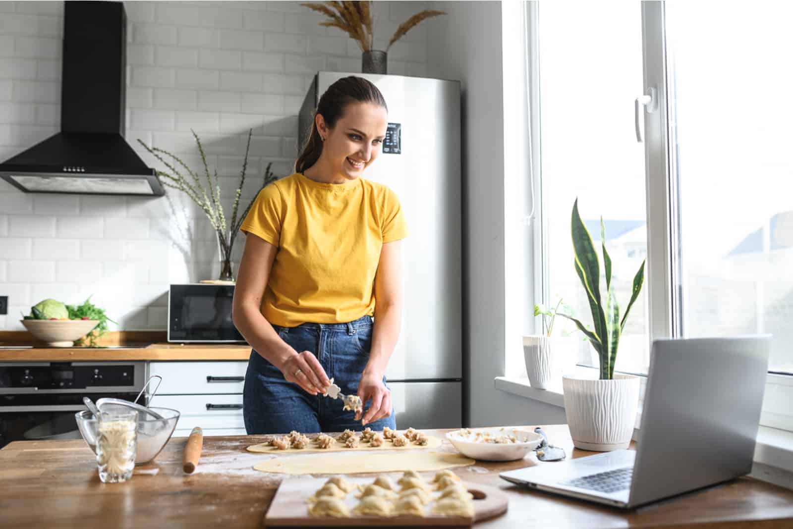 a smiling woman cooks and talks on a laptop