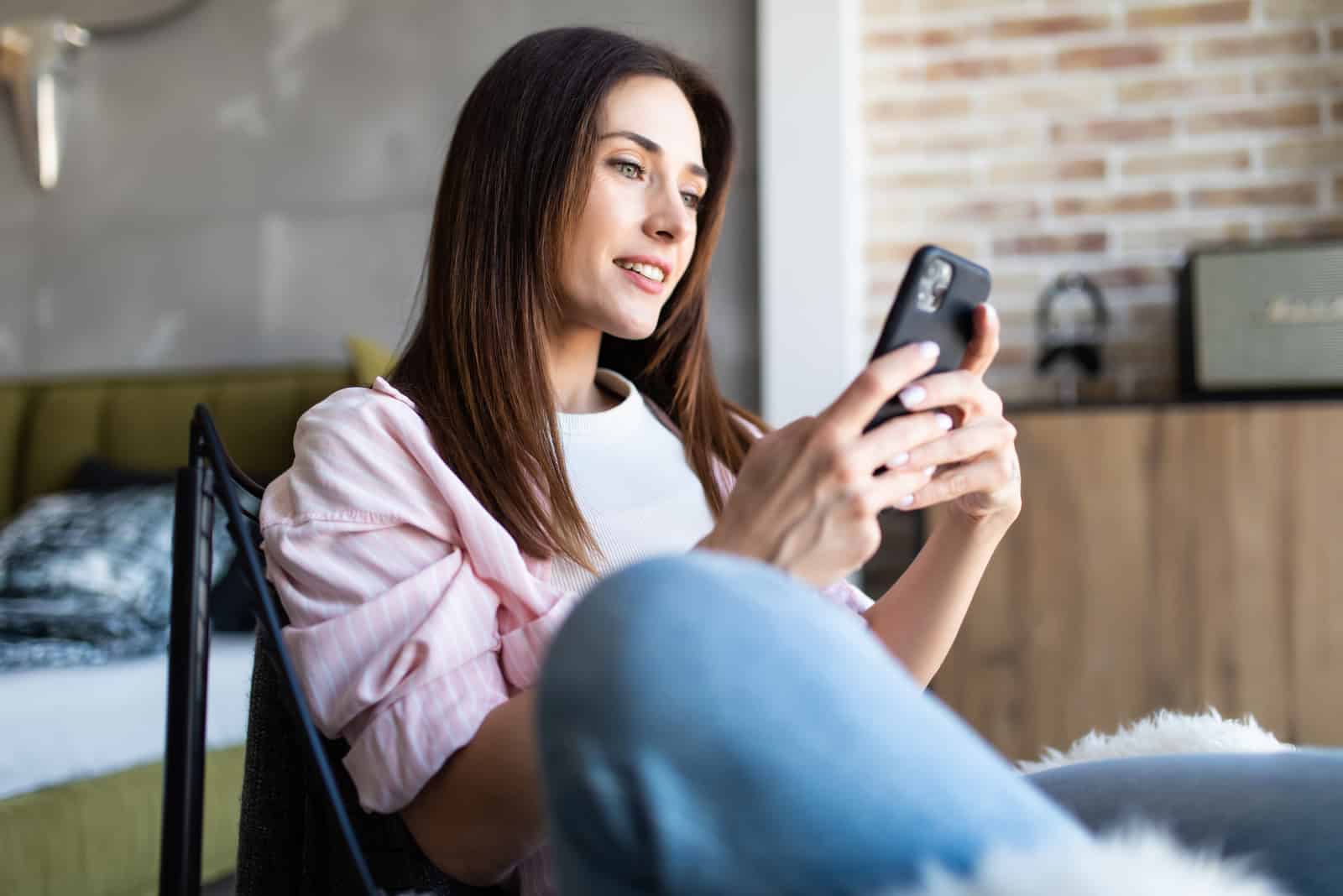 uma mulher sorridente sentada numa cadeira e a premir um telefone