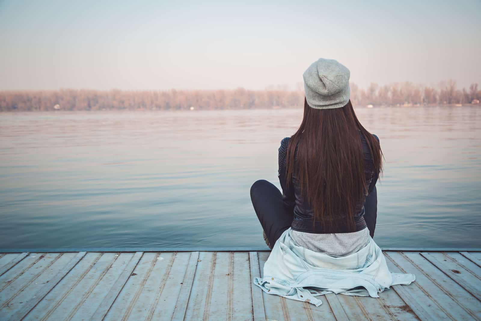 a woman with a hat on her head sits on a pier