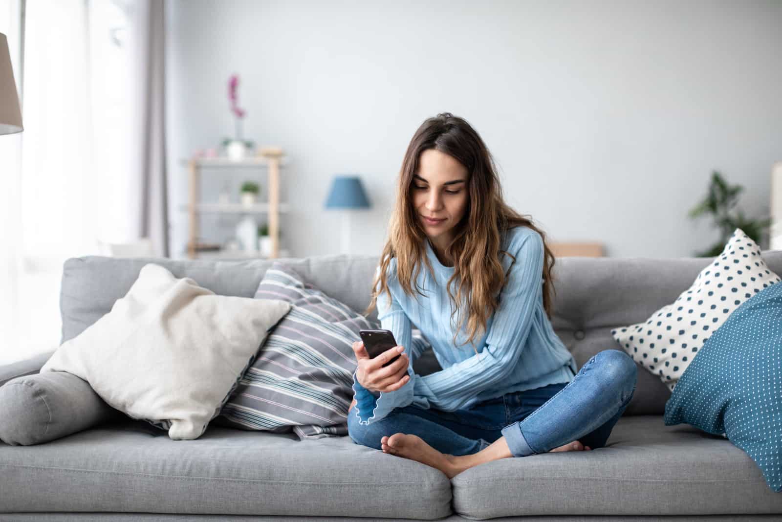 a woman with long brown hair sits on a couch and a button on a laptop