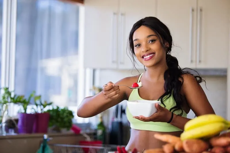 adult woman eating berry wearing athletic wear inside the kitchen
