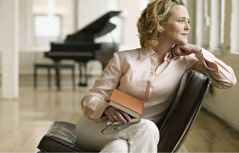 adult woman thinking sitting with a book at her lap and a piano at a distance