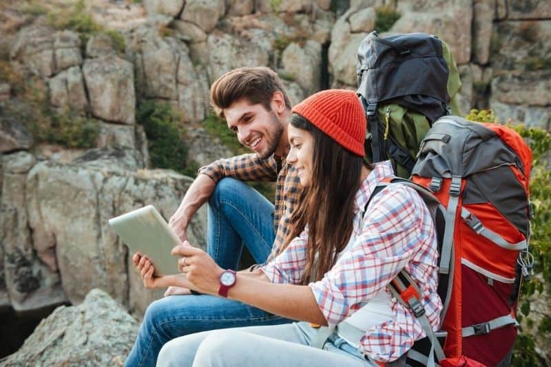 casal de aventureiros que pára de fazer caminhadas e olha para o seu tablet