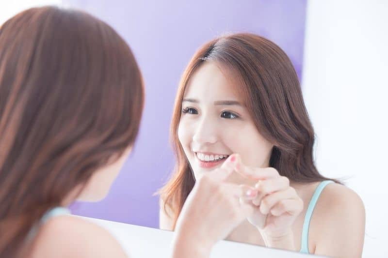 mulher asiática a olhar para si própria ao espelho, sorrindo e apontando para o espelho