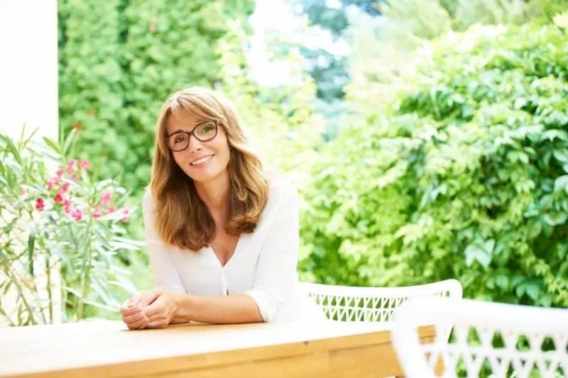 beautiful middle aged woman sitting outdoors with greenery plants nearby