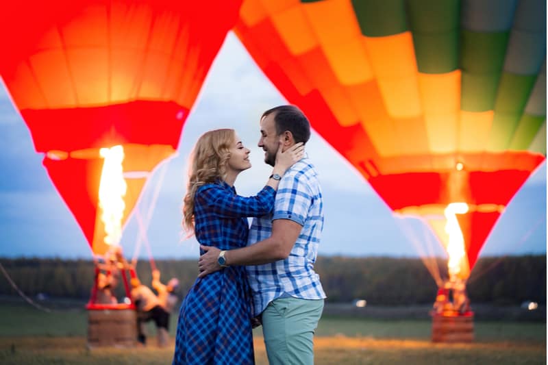 hermosa pareja dulce abrazando cerca del globo de aire caliente en el prado