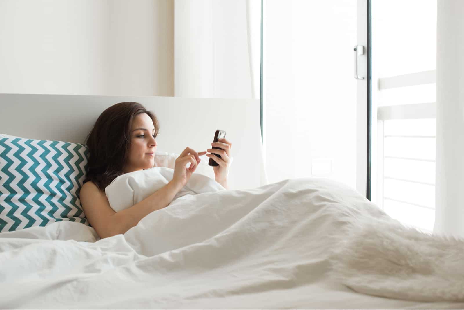 hermosa mujer acostada en la cama y la tecla en el teléfono