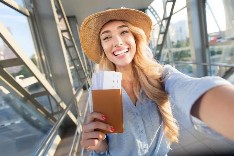 beautiful woman taking a selfie at the airport showing her passport