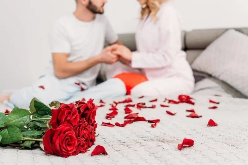 bed with rose petals with couple holding hands sitting on the bed