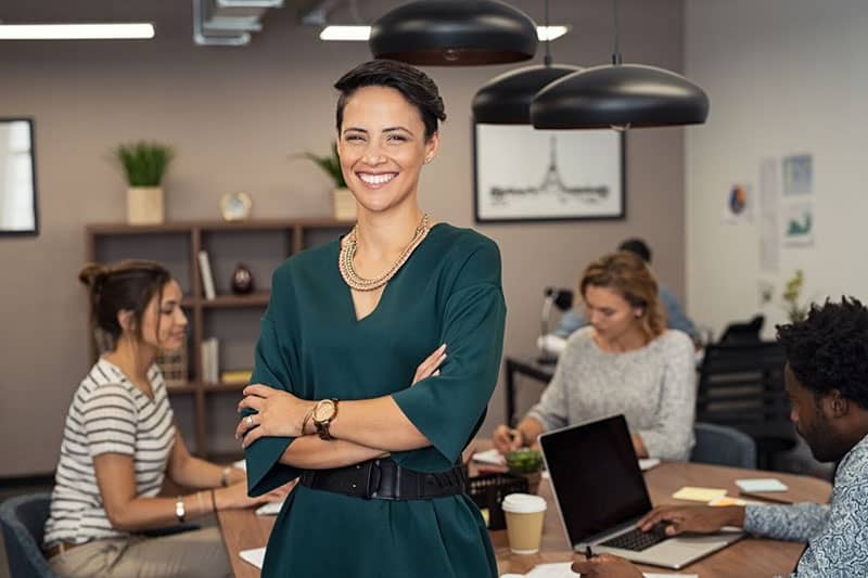 boss lady in green dress standing with workers working behind with their laptop