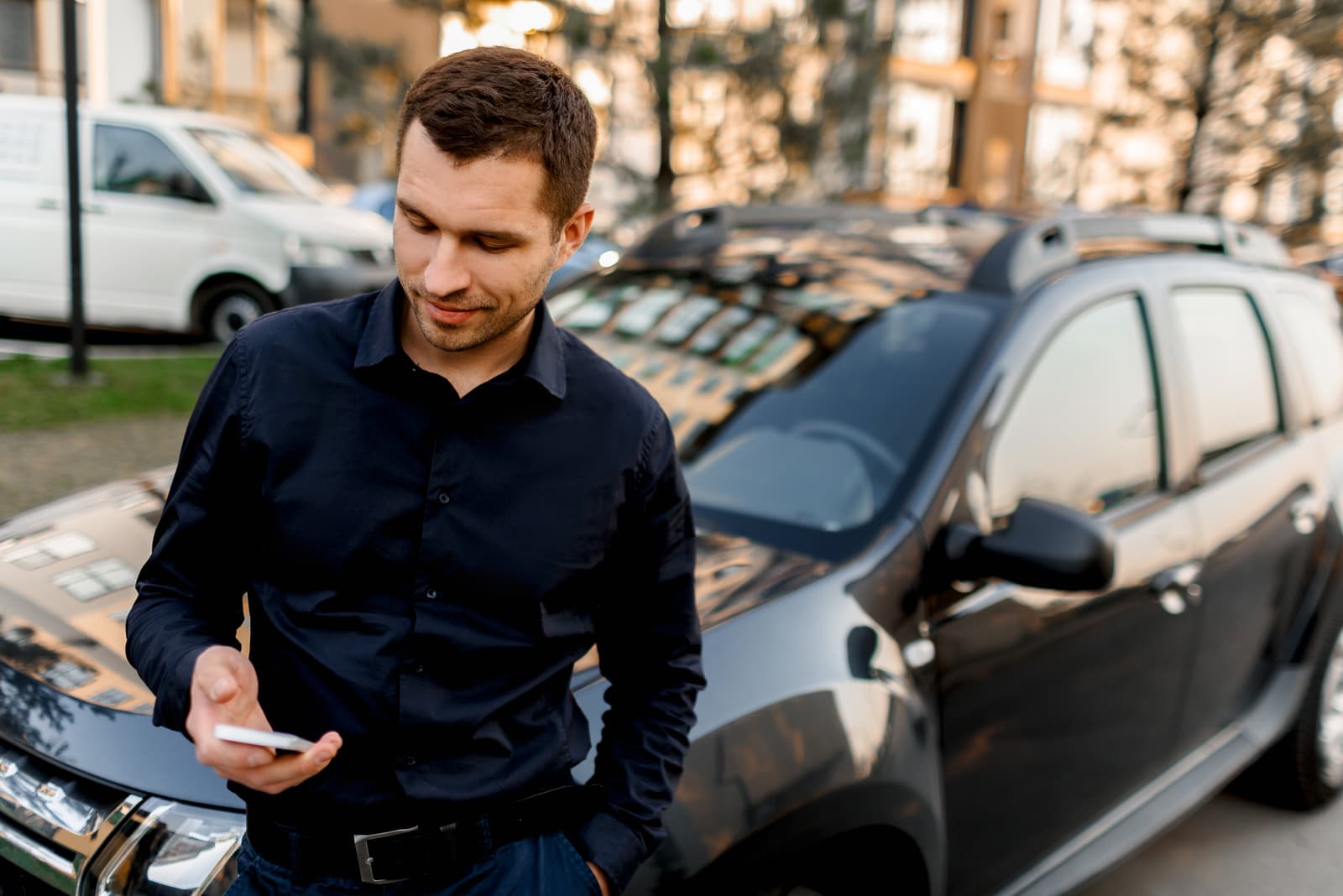 un hombre de negocios con camisa oscura se para en la calle cerca del coche