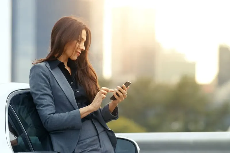 businesswoman checking phone while sitting in the bench outdoors