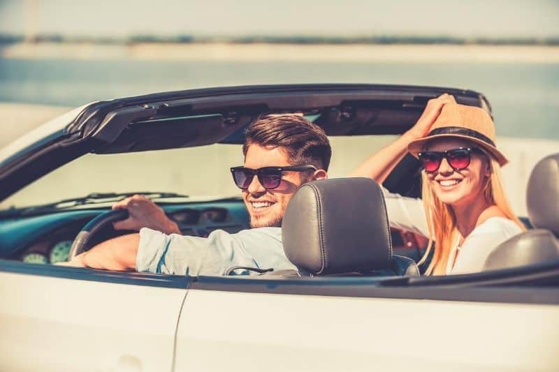 cheerful young couple riding in their convertible car