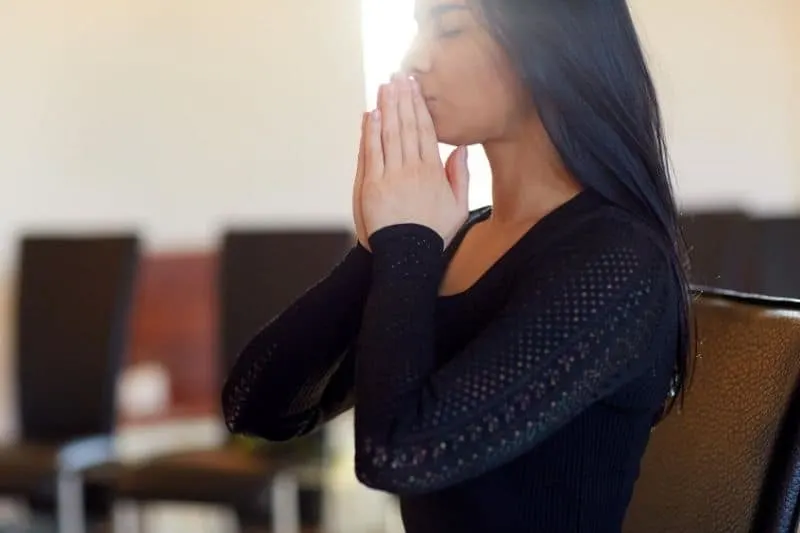 close up of sad woman praying indoors wearing black top