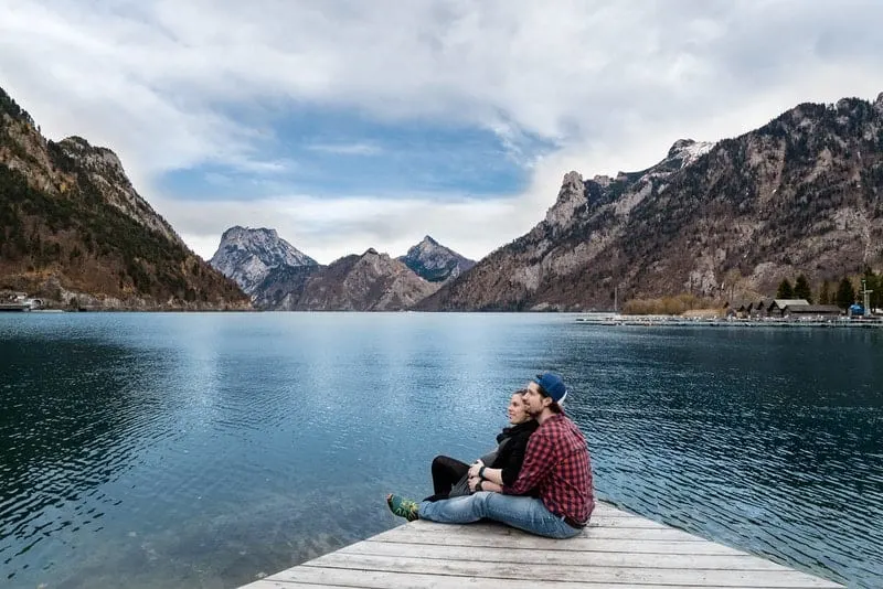 couple cuddling on a wooden platform on a lake with mountains nearby