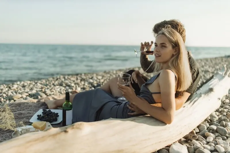 man and woman drinking wine while sitting near sea