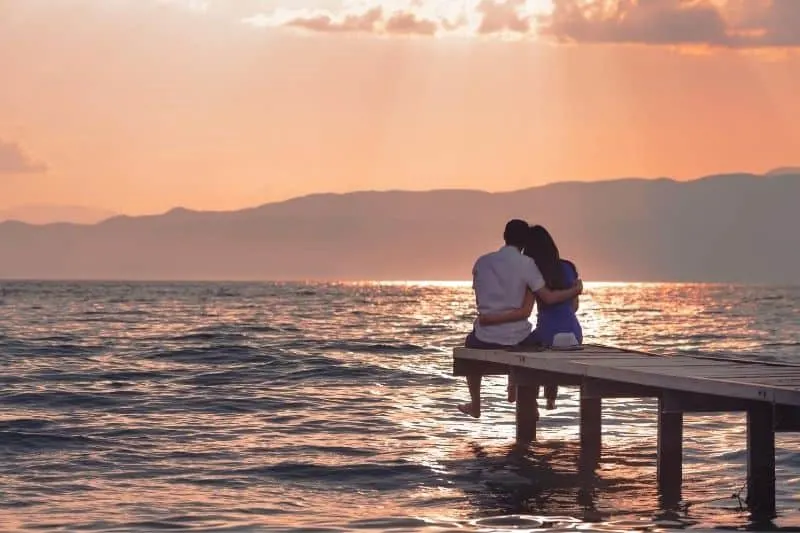 couple enjoying sunset sitting on the wooden platform on the sea