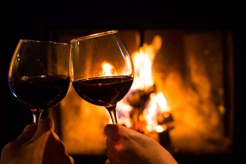 homem e mulher segurando copos de vinho perto da lareira