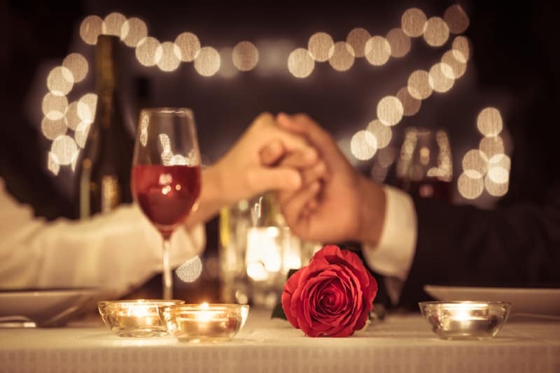 man and woman holding hands near red rose