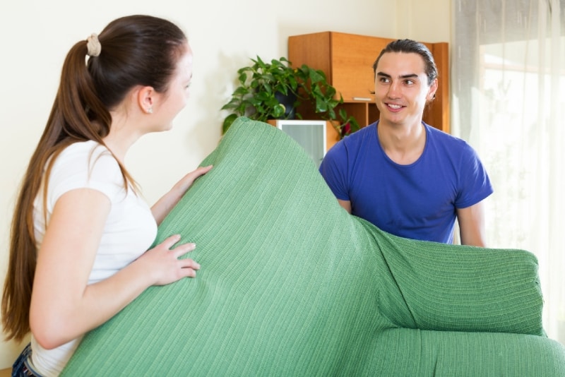 hombre y mujer sonrientes sosteniendo un sofá verde