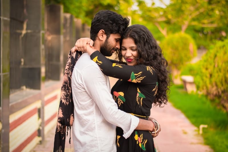 woman in black printed dress and man hugging outdoor