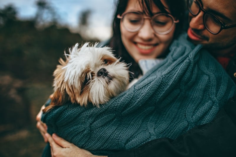 hombre y mujer con gafas abrazando perro al aire libre