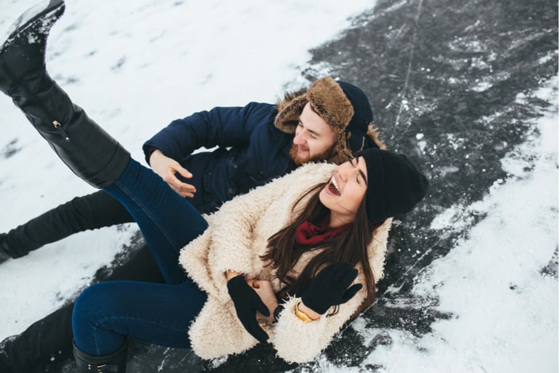 pareja patinando sobre hielo muriéndose de risa al caer sobre la nieve