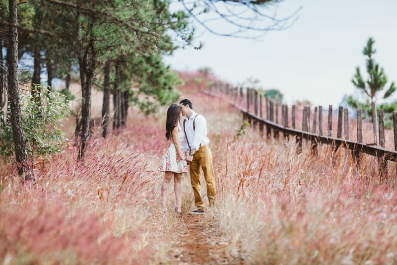 man and woman kissing while standing near trees