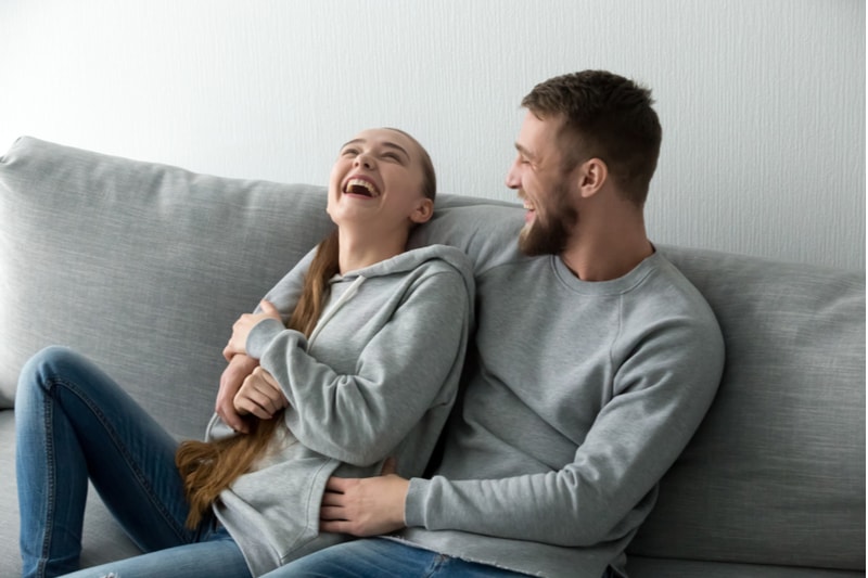 couple laughing together sitting on gray couch