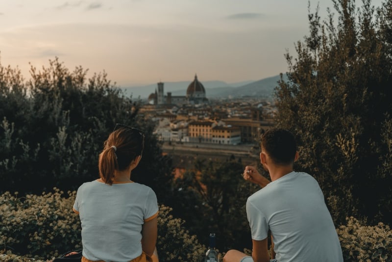 man and woman looking at city while sitting on grass