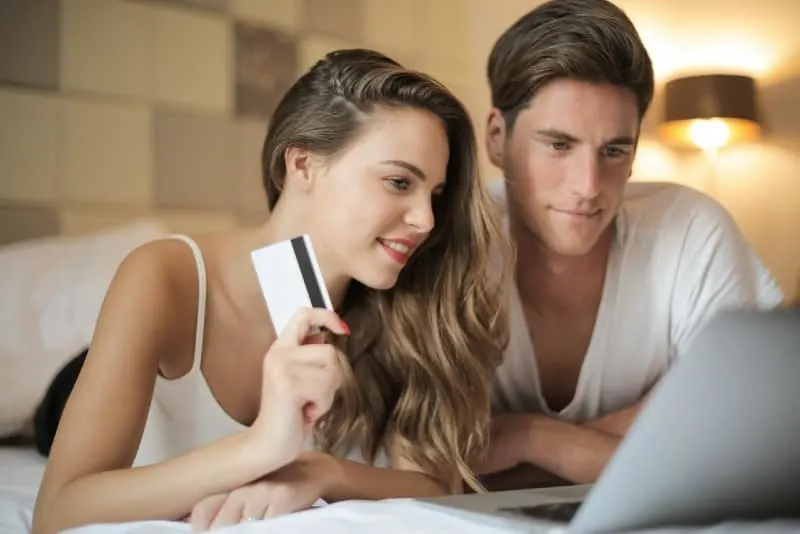 man and woman looking at laptop while lying on bed