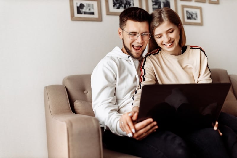 smiling man and woman looking at laptop while sitting on sofa