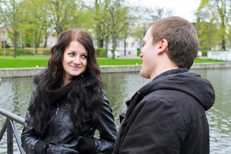 mujer con chaqueta negra y hombre haciendo contacto visual al aire libre