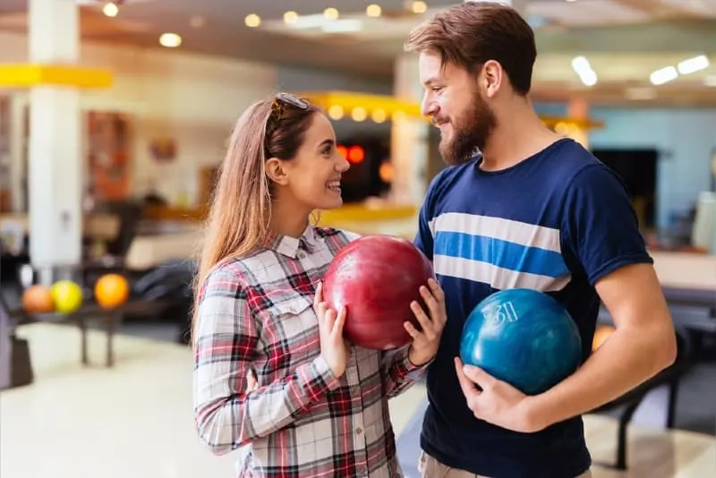 man and woman making eye contact while holding bowling balls