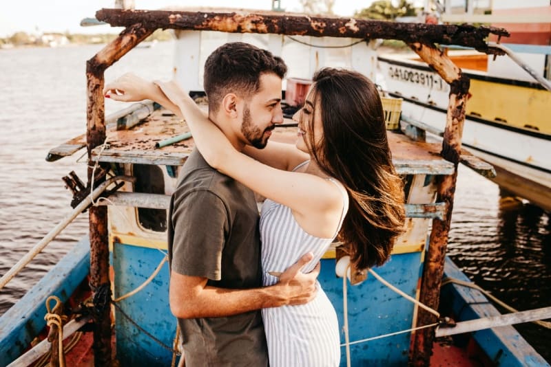 homem e mulher sorridentes estabelecem contacto visual enquanto se abraçam ao ar livre