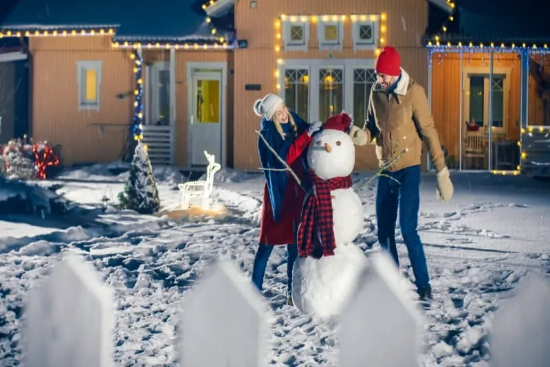 man and woman making snowman backyard