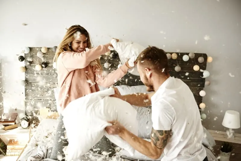 man and woman pillow fighting on bed