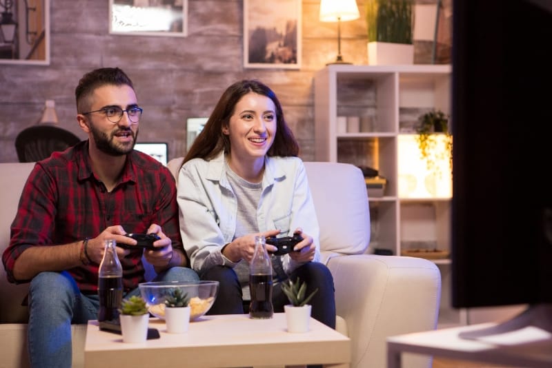 man and woman playing video games while sitting on sofa