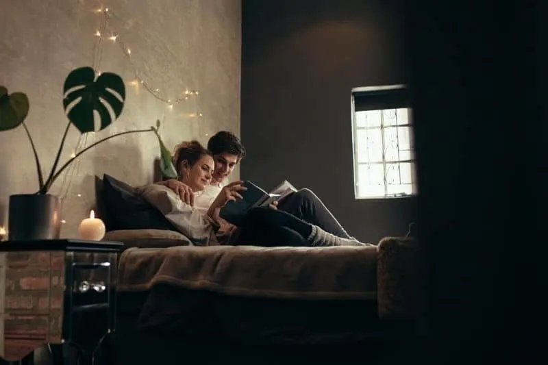 couple reading book together inside bedroom sitting in the bed