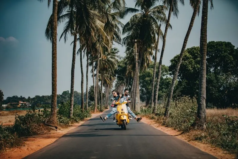man and woman riding on motorcycle near palm trees