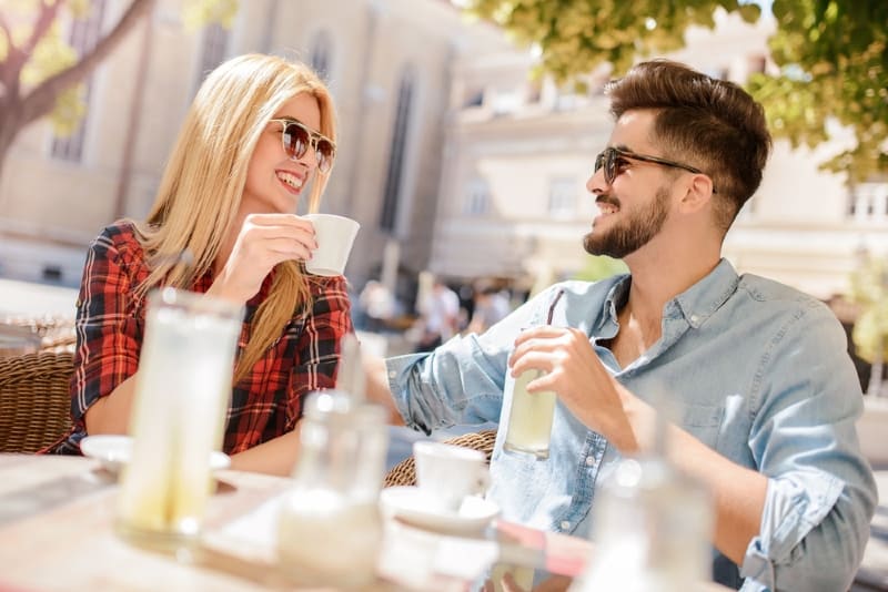 blonde woman with sunglasses and man sitting at table outdoor