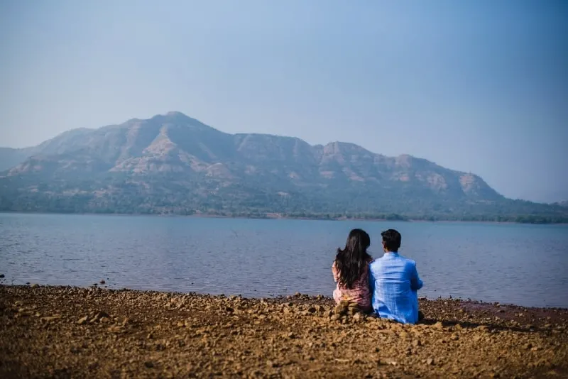 man with blue shirt and woman sitting near water