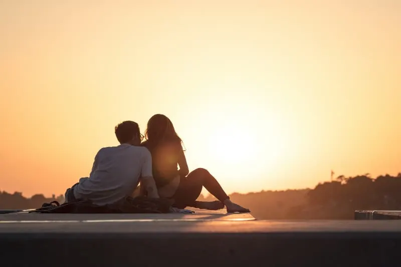 man and woman sitting on concrete surface during sunset