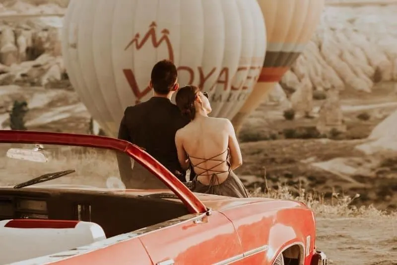 couple sitting on red coupe watching hot air balloon