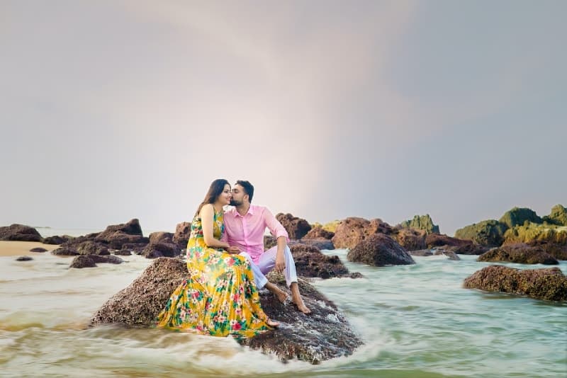 man kissing woman while sitting on rock