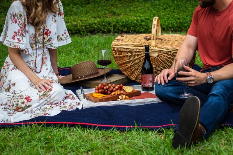 man and woman sitting on textile near picnic basket