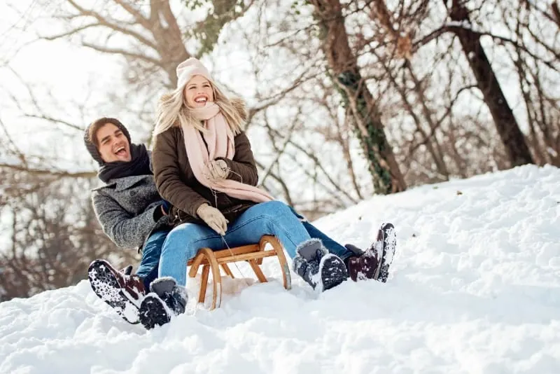 blonde woman with knit cap and man sliding on sled